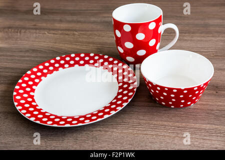 Red polka piastra tratteggiata, tazza e ciotola sul tavolo marrone Foto Stock