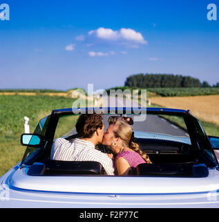 Vista posteriore della donna baciare il conducente durante la guida di una Mercedes convertibile auto sulla strada di campagna, Alsazia, Francia, Europa Foto Stock