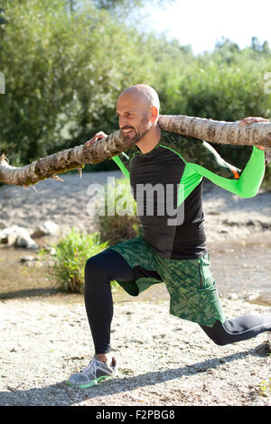 L'uomo facendo esercizio CrossFit con tronco di albero sulle sue spalle Foto Stock