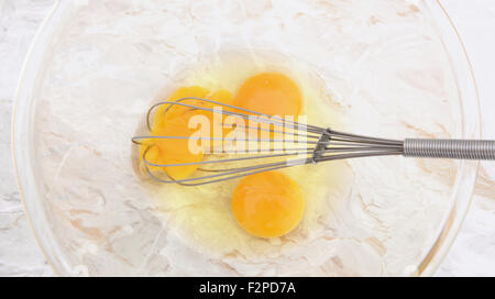 Battere tre uova con un filo di palloncino, frusta 1 tuorlo rotto, in una ciotola di vetro Foto Stock