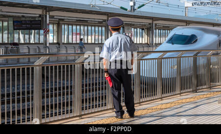 Un membro del personale di stazione di vegliare su una piattaforma mentre il treno superveloce Shinkansen passa Foto Stock