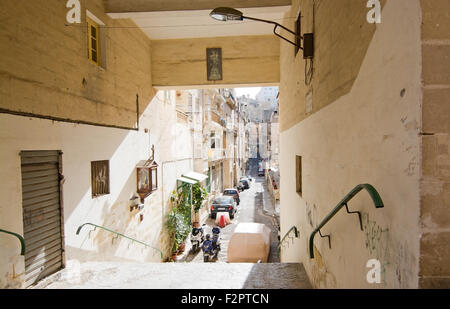 Città in scena per le strade de La Valletta con architettura e macchine parcheggiate al di sotto di una scala Foto Stock