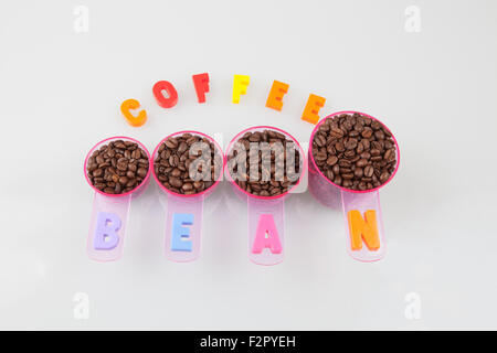 I chicchi di caffè in tazze di misura di varie dimensioni sul bianco. Foto Stock