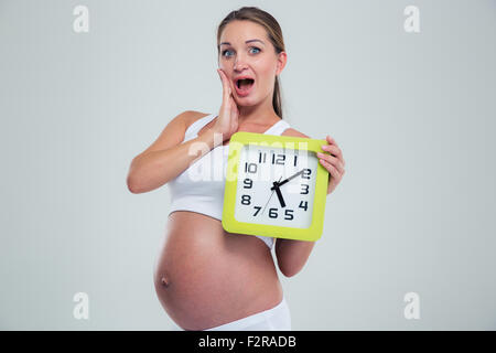 Ritratto di stupiti donna incinta azienda orologio da parete isolata su uno sfondo bianco Foto Stock