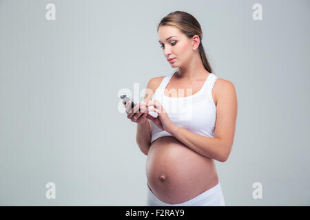 Ritratto di una donna in stato di gravidanza utilizza lo smartphone su sfondo grigio Foto Stock