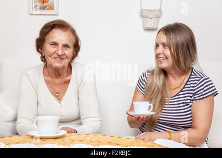 Accompagnatore avente una tazza di tè con un anziano pensionato donna Foto Stock