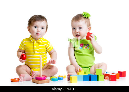 Due adorabili bambini che giocano con i giocattoli. I bimbi a ragazzo e una ragazza seduta sul pavimento. Isolato su sfondo bianco. Foto Stock