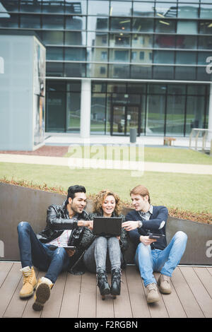 Multirazziale la gente di affari di lavoro seduta esterna sul terreno, collegato con dispositivi tecnologici come tablet e laptop, Foto Stock