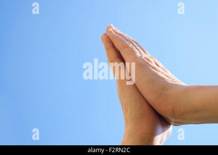 Donna con le mani in mano a pregare contro un cielo blu sullo sfondo. Foto Stock