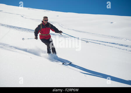 Una persona discese sugli sci fuori pista su pendio nevoso nelle Alpi italiane, con luminosa giornata di sole della stagione invernale. Polvere densa s Foto Stock