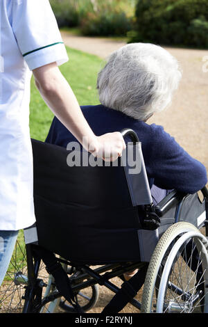 Chiusura del caregiver spingendo Senior donna in sedia a rotelle Foto Stock