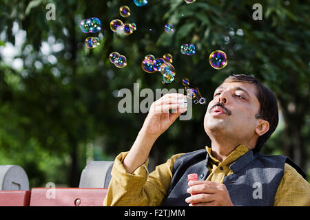 1 indian uomo adulto parco banco seduta GIOCA Bubble Wand Foto Stock