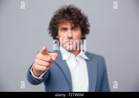 Ritratto di un imprenditore serio puntare il dito in telecamera su sfondo grigio. La messa a fuoco a portata di mano Foto Stock