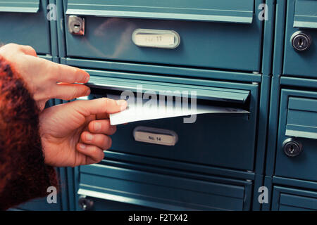 Primo piano su una mano femminile mettendo una lettera in una buca delle lettere Foto Stock