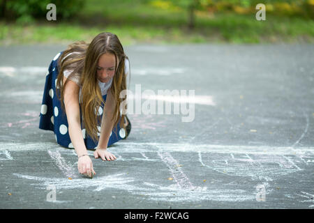 Teen girl il disegno con il gesso sulla pavimentazione. Foto Stock