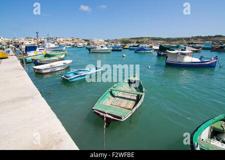 Verniciato colorato di piccole imbarcazioni ormeggiate nelle limpide acque turchesi di Marsaxlokk, Malta. Foto Stock