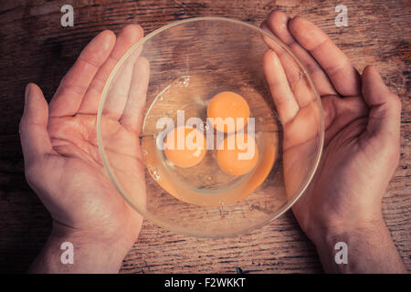 Mani tenendo una ciotola con tre uova crude in esso Foto Stock