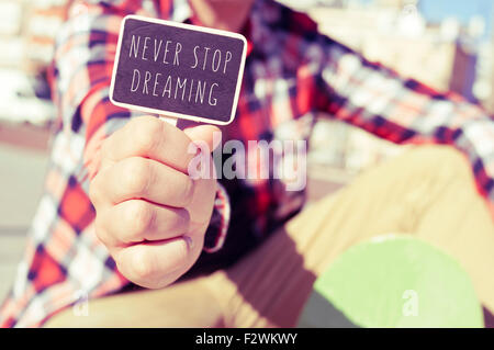 Primo piano di un giovane pattinatore uomo mostrando un cartello con scritto il testo non smette mai di sognare Foto Stock