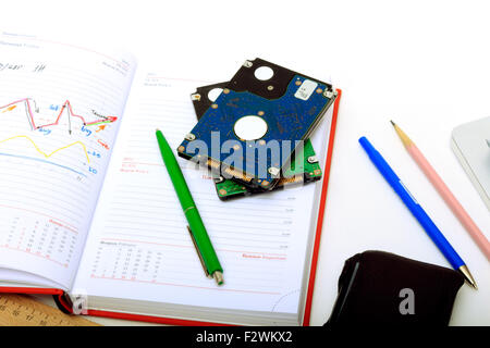 Tabelle finanziarie nel notebook. Su un tavolo bianco diario, telefono, dischi rigidi e forniture di cancelleria. Foto Stock