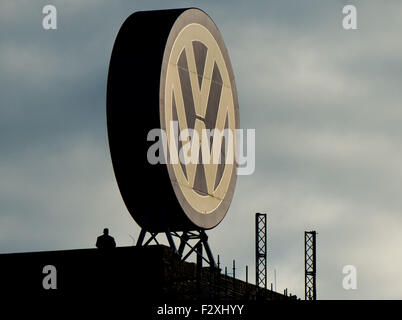 Un uomo si erge accanto ad un grande logo aziendale di Volkswagen illuminato dalla luce del mattino presso lo stabilimento della casa automobilistica tedesca a Wolfsburg, in Germania, il 25 settembre 2015. Foto: JULIAN STRATENSCHULTE/dpa Foto Stock