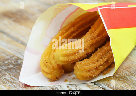 Lo spagnolo churros in sacchetto di carta su rustiche superficie in legno, primo piano Foto Stock