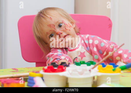 A 16 mesi, capelli biondi, caucasica, ragazza che gioca con vernici e un pennello mentre è seduto dentro a un piccolo tavolo. Foto Stock