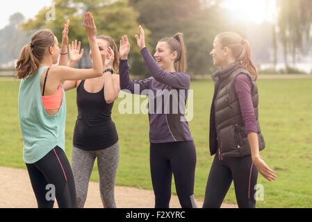 Quattro felici donne sane dando il doppio ad alta cinque gesto durante i momenti di relax dopo un esercizio all'aperto presso il parco. Foto Stock