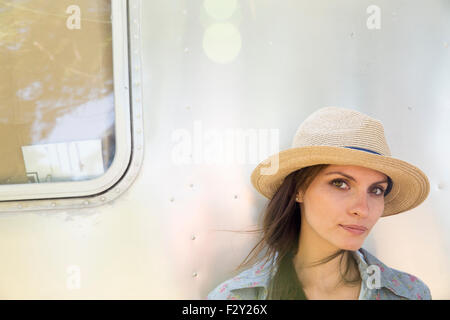 Una giovane donna che indossa un cappello seduti all'ombra di un color argento di rimorchio. Foto Stock