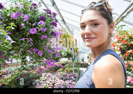 Una donna in piedi circondato da piante in fiore in una serra commerciale. Foto Stock