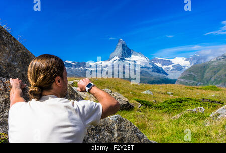 Un scalatore di pietra lo controlla il suo orologio intelligente guardando verso monte Cervino, Svizzera. Foto Stock