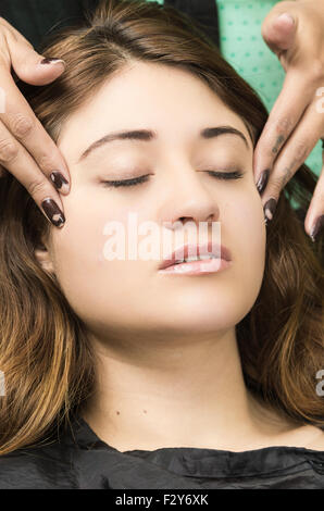 Closeup headshot brunette ottenere il trattamento di trucco dal parrucchiere professionista dando il massaggio del viso Foto Stock