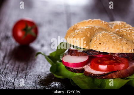 Gustoso panino farcito con prosciutto e verdure su sfondo di legno Foto Stock