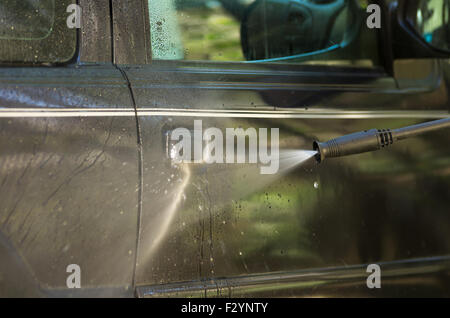 Il braccio con il guanto giallo tenendo alta pressione filtro acqua e di utilizzare la portiera della macchina windows. Foto Stock