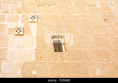 Croce di Malta decorazioni murali e finestra sul vecchio muro di Mdina, Malta. Foto Stock