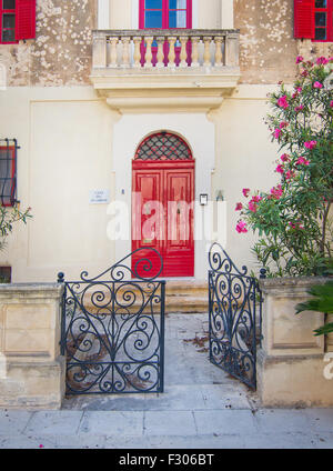 Bellissimo edificio residenziale all'interno di Mdina parete con porte rosse, balcone, persiane alle finestre e ingresso in nero ferro battuto. Foto Stock