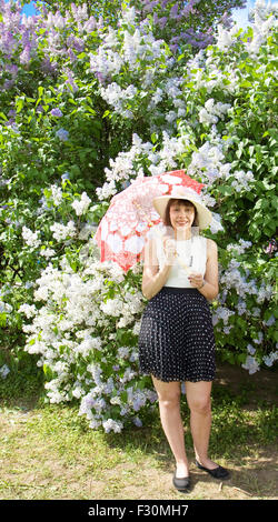 Bella Signora, brunette, europea, in cappello bianco camicia bianca e gonna nera con bianco-rosso ombrello nei pressi di Lilla. Foto Stock