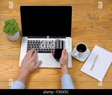 Elevato angolo di visualizzazione dei maschi di mano azienda cellulare durante la digitazione sulla tastiera del computer sul desktop. Foto Stock