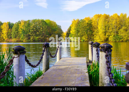 Vista sul molo di pietra con la colonna e la catena al lago e alberi colorati in giornata di sole in autunno Foto Stock