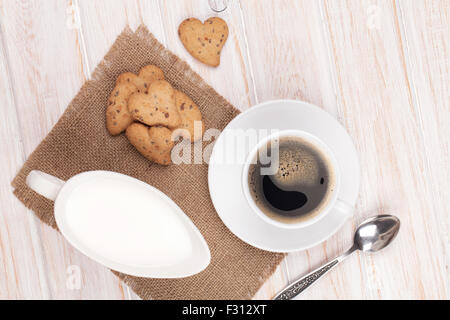 Tazza da caffè, a forma di cuore ad gingerbread cookie e la brocca del latte. Su bianco tavolo in legno Foto Stock