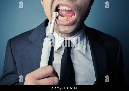 Giovane imprenditore sta spazzolando i suoi denti con uno spazzolino da denti elettrico Foto Stock