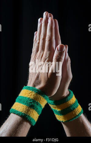 Mani atleta che indossa il Brasile di colore giallo e verde di braccialetti tenuti insieme nella preghiera contro uno sfondo scuro Foto Stock