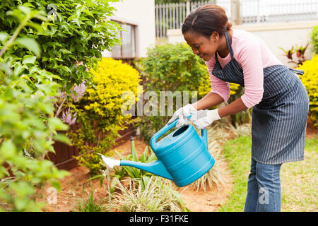 Felice giovane donna africana innaffiando le sue garden Foto Stock