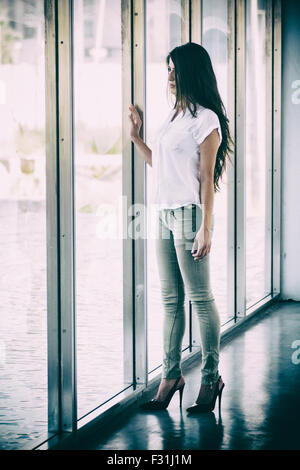 Giovane donna in piedi dalla finestra Foto Stock