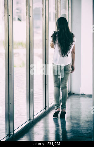 Giovane donna in piedi dalla finestra Foto Stock