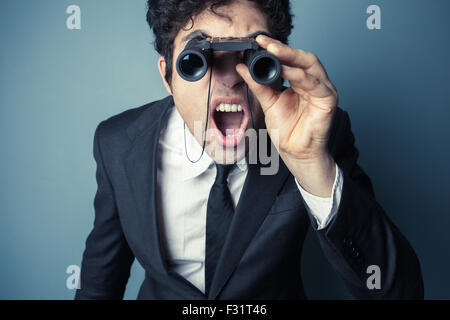 Giovane imprenditore è guardare attraverso il binocolo ed è sorpreso da ciò che vede Foto Stock