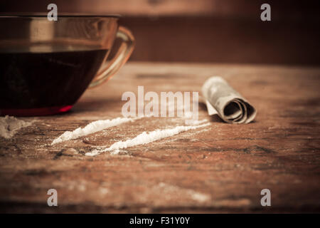 Una tazza di caffè con linee di cocaina e un arrotolato banconota accanto ad esso Foto Stock