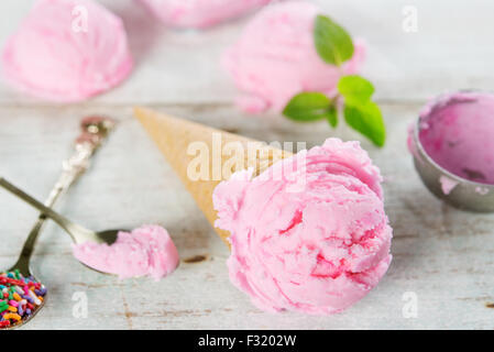 Rosa gelato in cono di cialda con utensile su legno rustico sfondo. Foto Stock