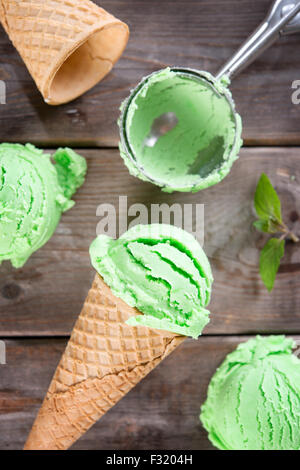 Vista superiore della menta gelato in una cialda coni con utensile sopra il vecchio in legno rustico sfondo vintage. Foto Stock