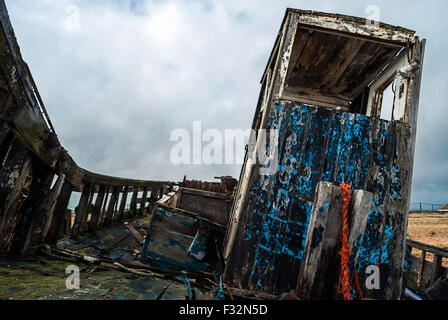Abbandonata la pesca in barca da sinistra a rot e degrado sulla spiaggia di Dungeness, Kent. Un grigio, moody sky aggiunge alla triste scena Foto Stock