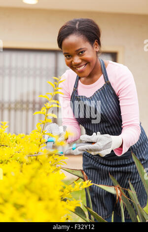 Attraente donna africana la potatura di piante nel suo giardino Foto Stock